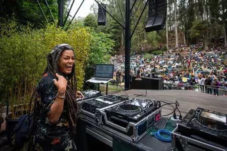 在斯特恩格罗夫音乐节(Stern Grove Festival)上，一位女DJ从背后看着镜头，对着镜头微笑。.